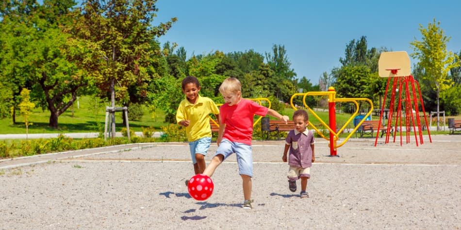 Three young children kicking a ball on a playground